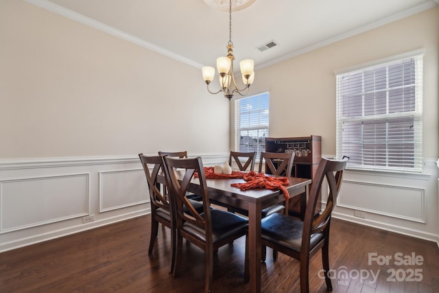 dining area featuring visible vents, ornamental molding, wainscoting, wood finished floors, and a chandelier