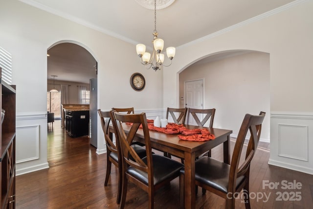 dining room with dark wood-style flooring, wainscoting, crown molding, and a decorative wall