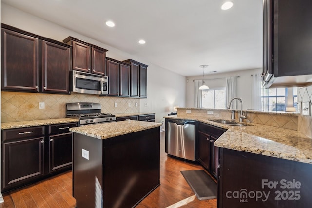 kitchen featuring stainless steel appliances, wood finished floors, a sink, light stone countertops, and tasteful backsplash