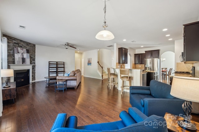 living area featuring arched walkways, a fireplace, dark wood-style floors, and visible vents