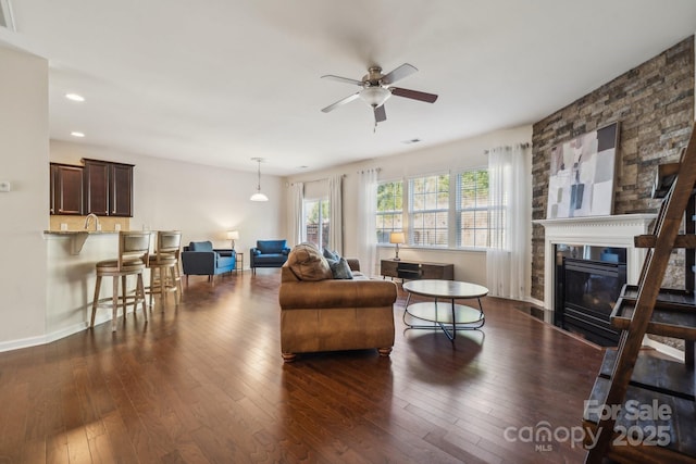 living area featuring a large fireplace, ceiling fan, dark wood finished floors, and recessed lighting