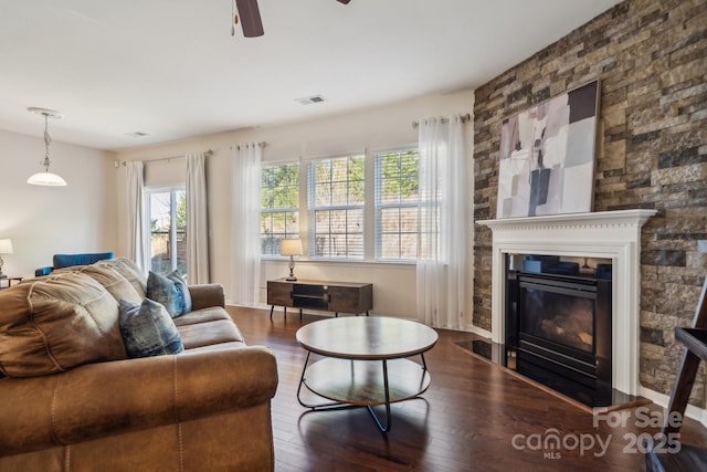 living area with visible vents, dark wood-type flooring, a glass covered fireplace, ceiling fan, and baseboards