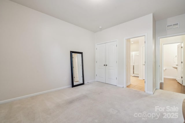 unfurnished bedroom featuring ensuite bathroom, light colored carpet, visible vents, baseboards, and a closet