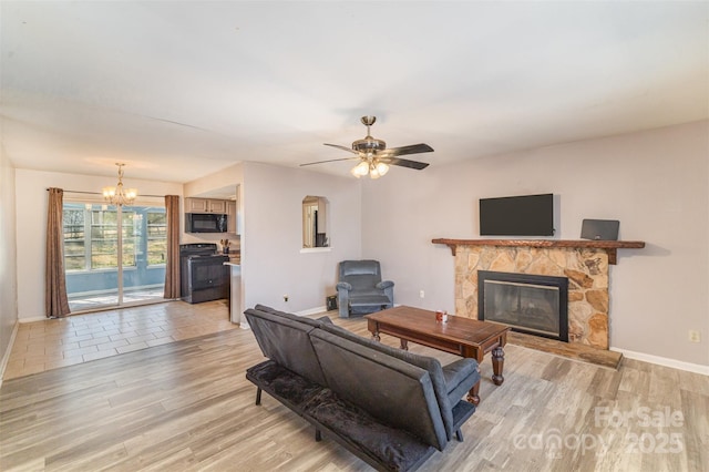 living area with light wood finished floors, baseboards, ceiling fan with notable chandelier, and a stone fireplace