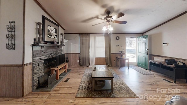 living room with crown molding, light wood-style flooring, a stone fireplace, and wainscoting