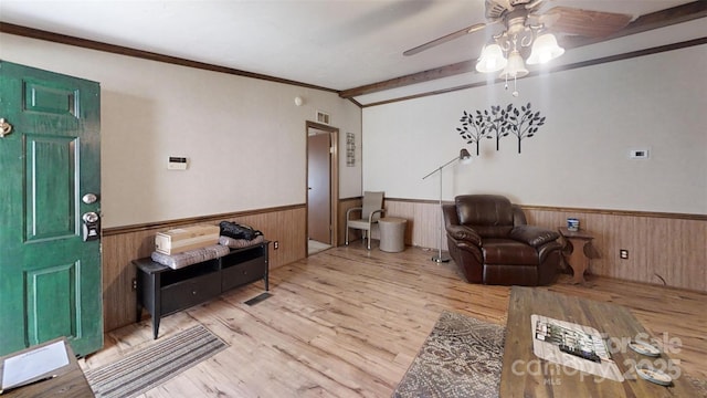 living room featuring light wood-style floors, a wainscoted wall, crown molding, and a ceiling fan