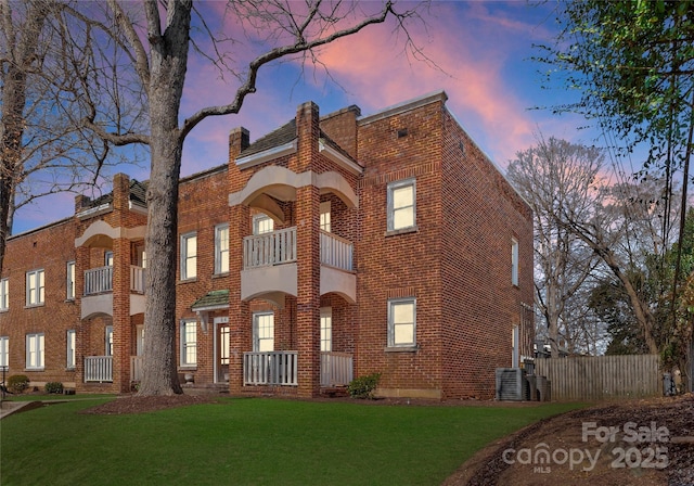 view of front of property with brick siding, a yard, a balcony, and fence