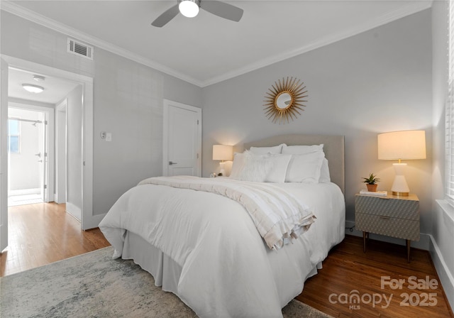 bedroom with baseboards, crown molding, visible vents, and wood finished floors