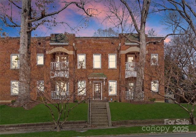 view of front of home with a yard, brick siding, and a balcony