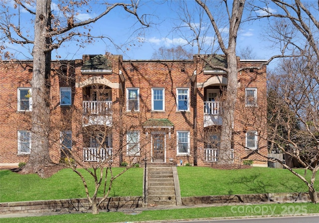 view of front of property featuring brick siding, a front lawn, and a balcony