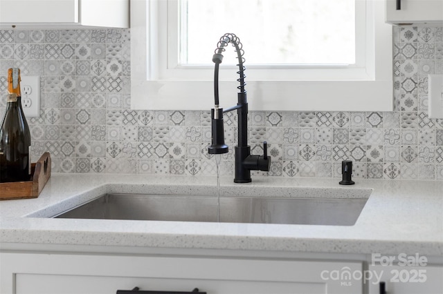 room details with tasteful backsplash, light stone counters, white cabinets, and a sink