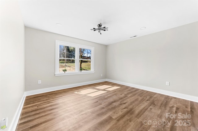 empty room with wood finished floors, visible vents, and baseboards