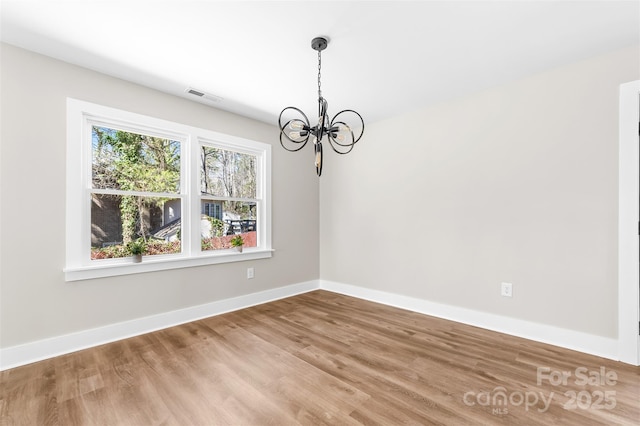 empty room featuring baseboards, wood finished floors, visible vents, and a notable chandelier