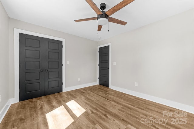 unfurnished bedroom with a closet, wood finished floors, a ceiling fan, and baseboards