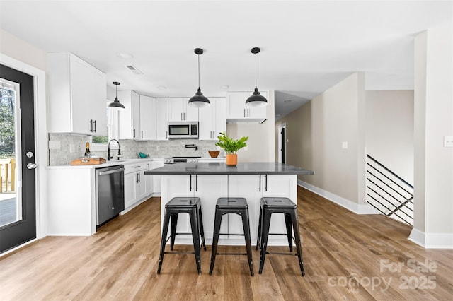 kitchen with stainless steel appliances, wood finished floors, visible vents, white cabinets, and decorative backsplash