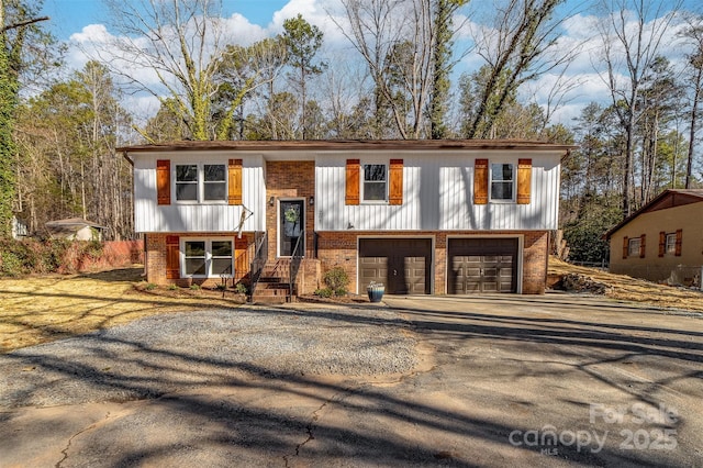 raised ranch featuring driveway, a garage, and brick siding