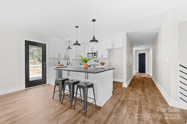 kitchen with white cabinets, a kitchen breakfast bar, light wood finished floors, stainless steel microwave, and tasteful backsplash