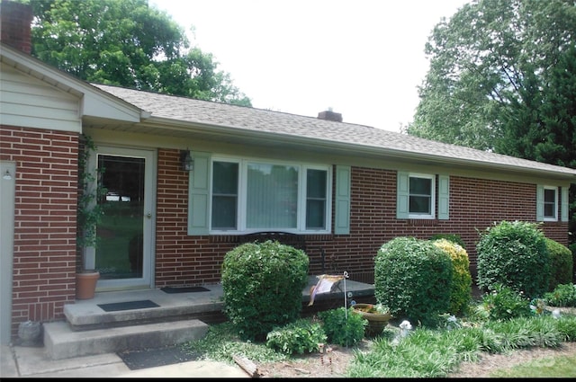 exterior space featuring roof with shingles, a chimney, and brick siding