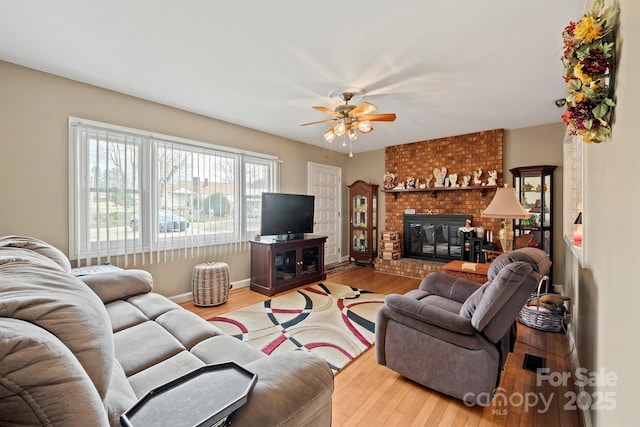 living room featuring ceiling fan, a fireplace, baseboards, and wood finished floors