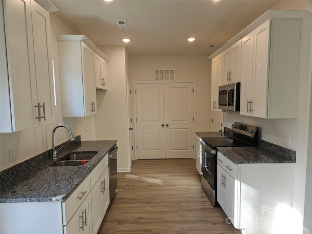 kitchen with white cabinets, dark stone countertops, stainless steel appliances, and a sink