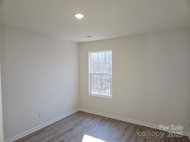 spare room featuring wood finished floors, visible vents, and baseboards