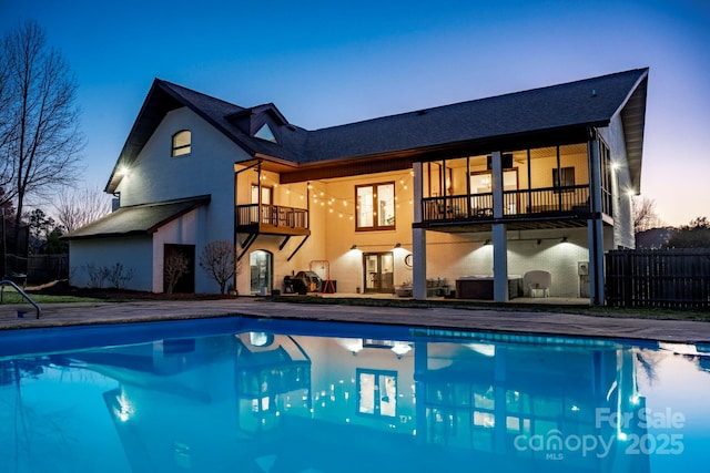 rear view of property featuring a patio, fence, a balcony, and a fenced in pool