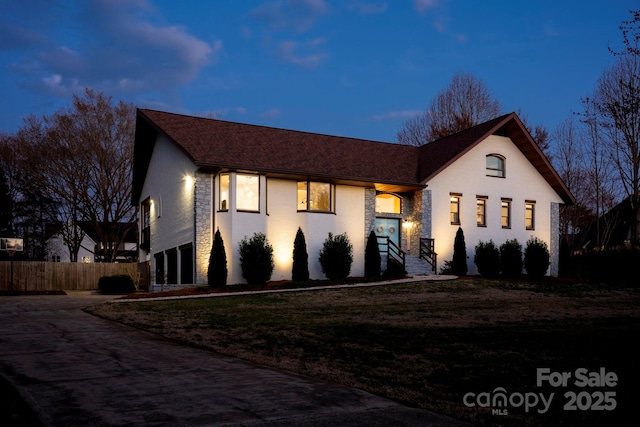 view of front of home featuring an attached garage, fence, stone siding, driveway, and a front lawn