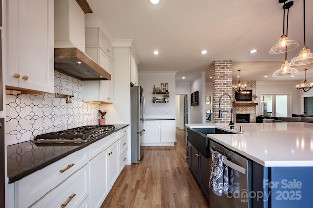 kitchen with a sink, open floor plan, wall chimney range hood, appliances with stainless steel finishes, and crown molding