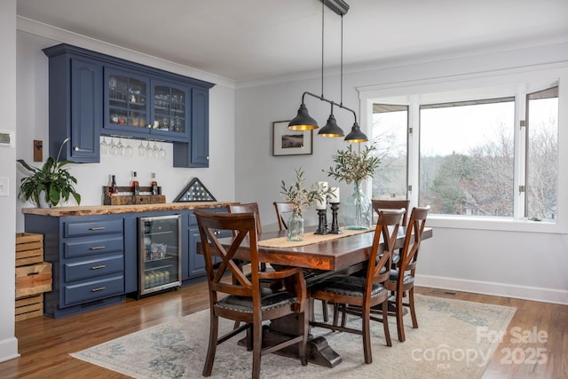 dining area featuring a bar, beverage cooler, crown molding, and wood finished floors