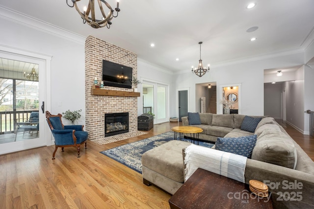 living area featuring wood finished floors, an inviting chandelier, crown molding, a brick fireplace, and recessed lighting