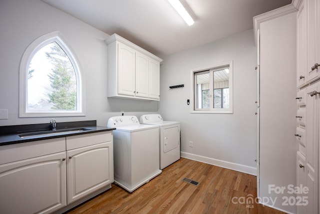 washroom featuring washer and clothes dryer, a wealth of natural light, cabinet space, light wood-style floors, and a sink