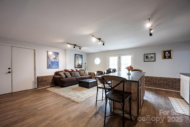 dining area with dark wood-style floors, brick wall, wainscoting, and rail lighting