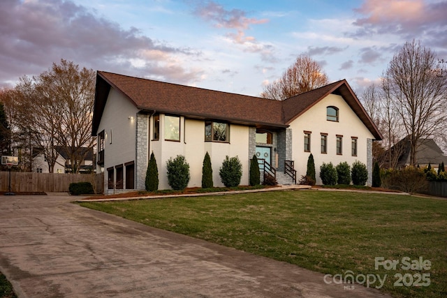 view of front of property with an attached garage, a front yard, fence, stone siding, and driveway