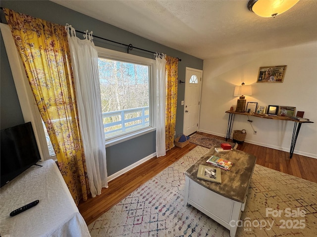 living area with a textured ceiling, wood finished floors, and baseboards