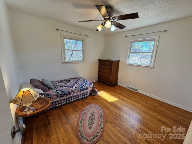 bedroom featuring multiple windows, wood finished floors, visible vents, and baseboards