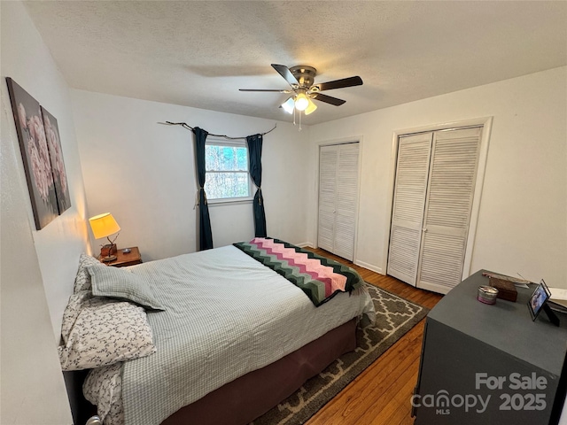 bedroom with a textured ceiling, a ceiling fan, multiple closets, and wood finished floors