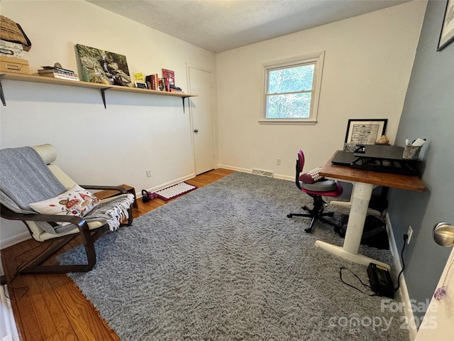 home office with a textured ceiling, wood finished floors, visible vents, and baseboards