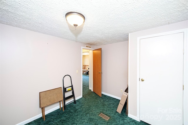 interior space with visible vents, baseboards, dark colored carpet, and a textured ceiling