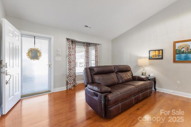 living area with visible vents, baseboards, wood finished floors, and vaulted ceiling