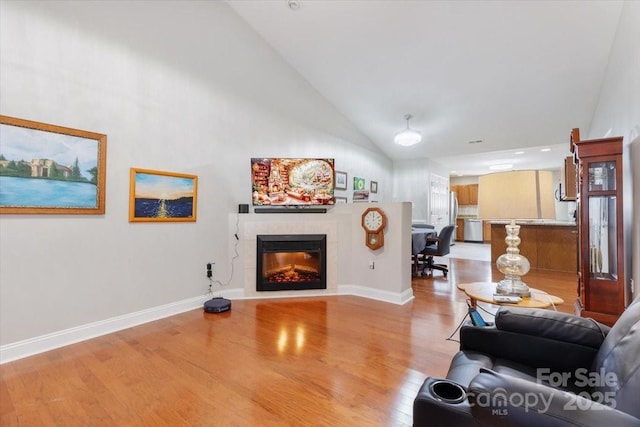 living area with a fireplace, baseboards, light wood finished floors, and high vaulted ceiling