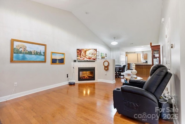 living area featuring a glass covered fireplace, light wood-style flooring, baseboards, and high vaulted ceiling