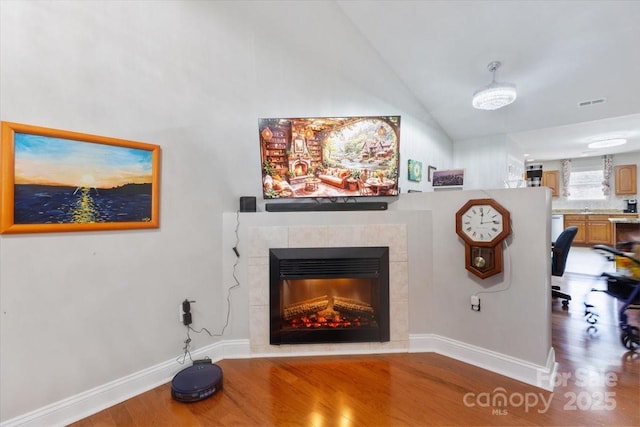 living area with wood finished floors, baseboards, visible vents, a fireplace, and vaulted ceiling