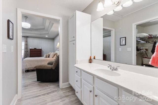 bathroom with a tray ceiling, wood finished floors, connected bathroom, crown molding, and vanity