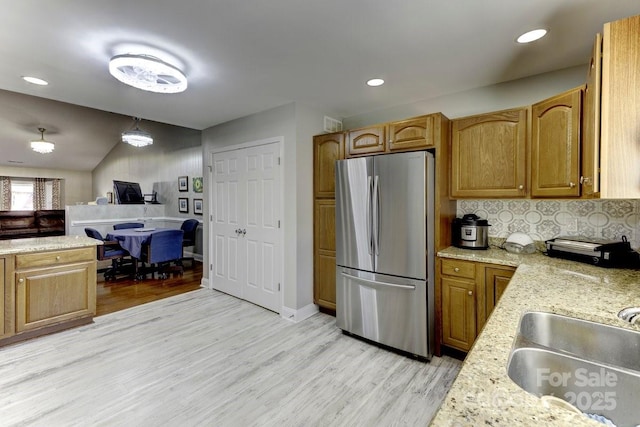 kitchen featuring light stone countertops, light wood-type flooring, freestanding refrigerator, and a sink