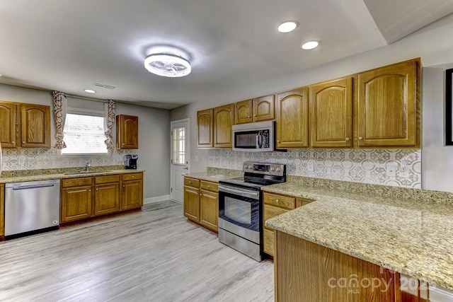 kitchen with brown cabinets, a sink, light wood-style floors, appliances with stainless steel finishes, and decorative backsplash