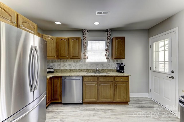 kitchen with tasteful backsplash, brown cabinets, light wood-style flooring, stainless steel appliances, and a sink