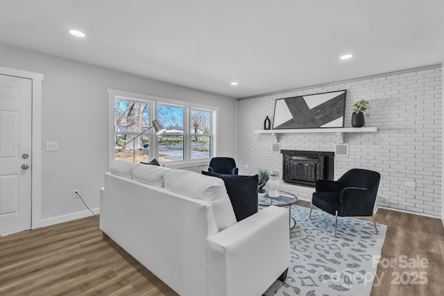 living area featuring brick wall, a brick fireplace, and wood finished floors