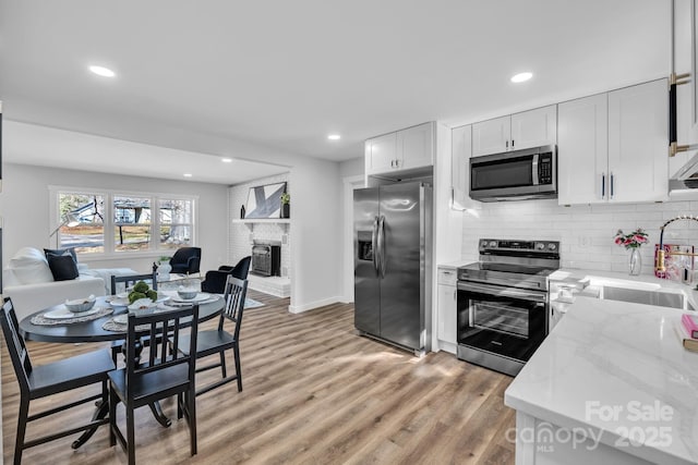 kitchen featuring white cabinets, appliances with stainless steel finishes, open floor plan, light wood-type flooring, and a sink