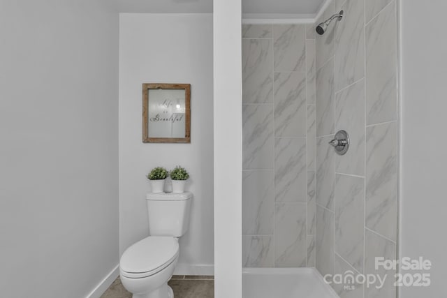 bathroom featuring tile patterned flooring, a tile shower, toilet, and baseboards