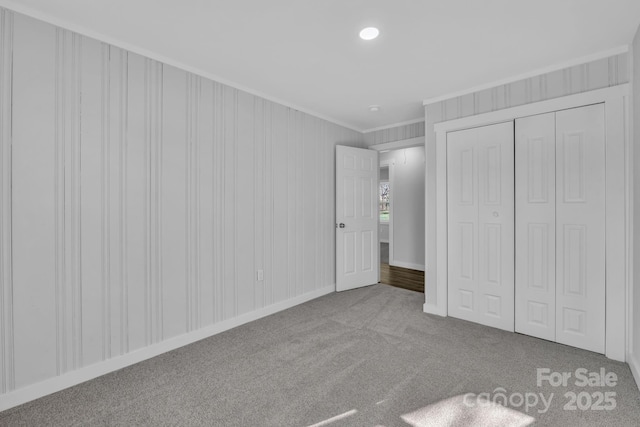 unfurnished bedroom with a closet, carpet flooring, crown molding, and baseboards